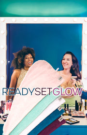 Photo of two women smiling in the mirror, in the foreground there are five Turbie Twist hair towels. The colors are pink, aqua, white, blue and purple. Text in the image reads "Ready Set Glow."